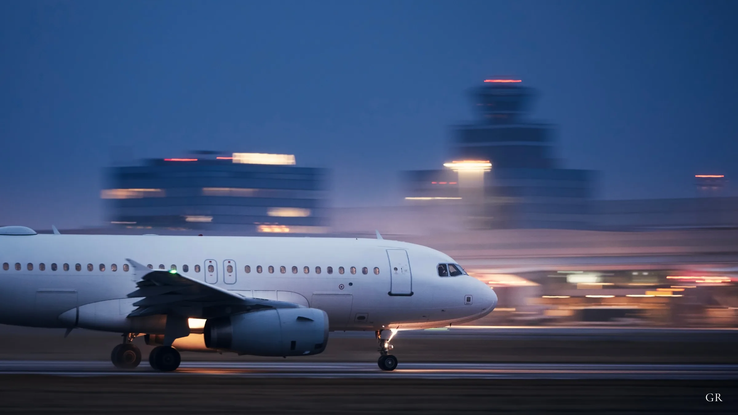 An Airbus A320 taxiing at dusk with the control tower behind it — GermanRide airport transfers across Germany