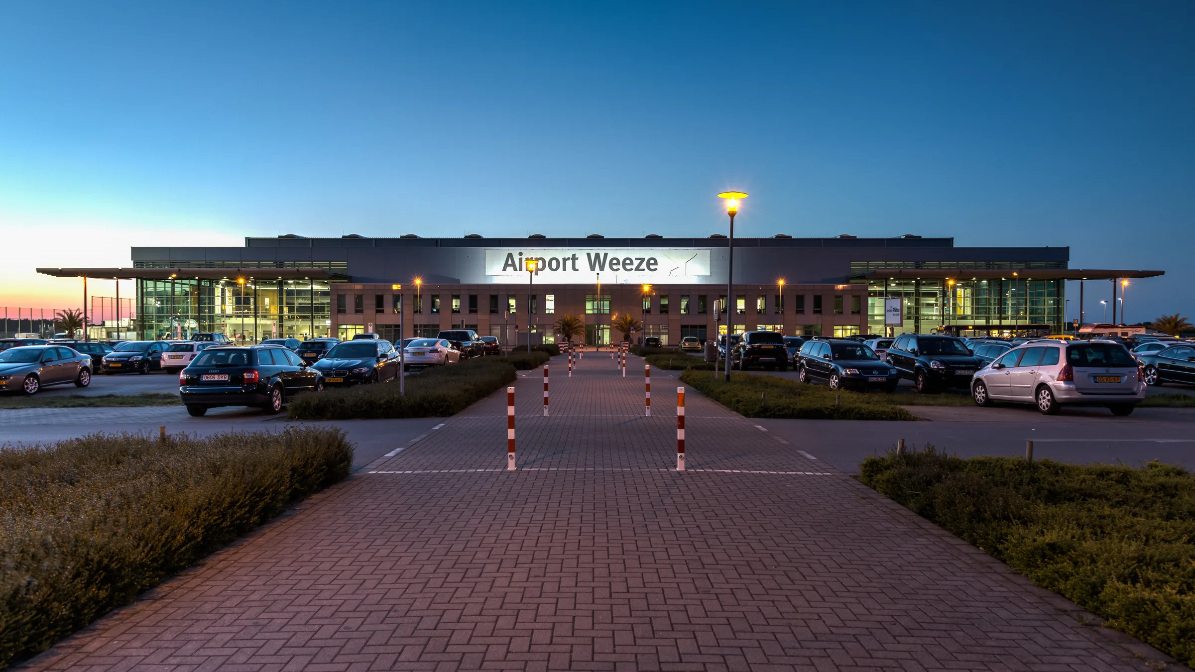 The lit Airport Weeze terminal frontage at dusk, seen across the car park
